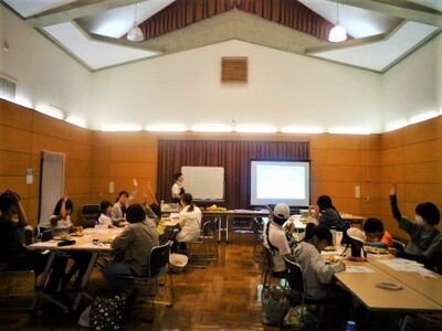 牧野先生が話しています。手を挙げている人がたくさんいます。